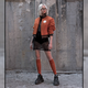 A model wears the burnt orange pilot jacket with a lace skirt and top, with knee-high burnt orange socks and black sneakers.
